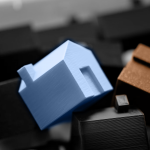 Blaues und oranges Miniaturhaus auf einem Haufen schwarzer und grauer Miniaturhäusern | Foto von © Jakub Zerdzicki